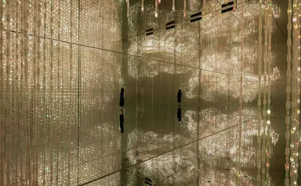 Two people standing in a mirrored room filled with hanging light installations, creating a mesmerizing display of reflections and lights.